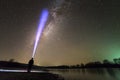 Back view of man with head flashlight standing on river bank, long blue beam across beautiful dark starry sky. Night photography Royalty Free Stock Photo