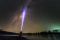 Back view of man with head flashlight standing on river bank, long blue beam across beautiful dark starry sky. Night photography Royalty Free Stock Photo