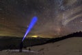 Back view of man with head flashlight standing on snowy valley under beautiful dark blue winter starry sky, bright blue beam on Royalty Free Stock Photo