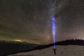 Back view of man with head flashlight standing on snowy valley under beautiful dark blue winter starry sky, bright blue beam on Royalty Free Stock Photo