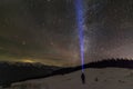 Back view of man with head flashlight standing on snowy valley under beautiful dark blue winter starry sky, bright blue beam on Royalty Free Stock Photo