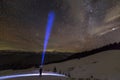 Back view of man with head flashlight standing on snowy valley under beautiful dark blue winter starry sky, bright blue beam on