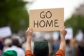 Back view of man holding up protest sign with text 'Go home