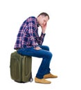 Back view of a man sitting on a suitcase.