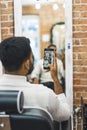 back view of a man taking a mirror selfie at the barbershop, vertical shot Royalty Free Stock Photo