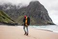 Back view of man tourist with backpack walking in front of the mountain massif while journey by ocean beach Royalty Free Stock Photo