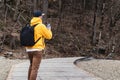 Back view. Man tourist in yellow hoodie with backpack stands outdoors, using smartphone. Traveler walks, takes photo on cell phone Royalty Free Stock Photo