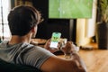 Back view of man watching football match and making bets at bookmaker's website in front of TV screen Royalty Free Stock Photo