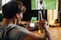 Back view of man watching football match and making bets at bookmaker's website in front of TV screen Royalty Free Stock Photo