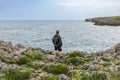 Back view of a mature man with backpack and casual clothes looking at the sea with his dog in nature. Royalty Free Stock Photo