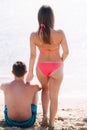 Back view of man sitting on the beach and woman put hand on his shoulder. On the back of a man and on the woman`s