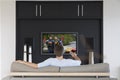 Back view of mid-adult man changing channels with television remote control in living room