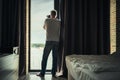 Back view of middle-aged gray-haired man photographer in a  taking picture using camera standing near open window of apartment Royalty Free Stock Photo