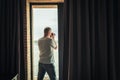 Back view of middle-aged gray-haired man photographer in a  taking picture using camera standing near open window of apartment Royalty Free Stock Photo