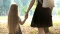 Back view of mom and her little daughter walking together holding hands in summer park Royalty Free Stock Photo
