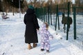 Back view of mother and child walking on a sunny frosty winter day in the park near outdoor zoo with llama