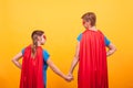 Back view of mother and her little girl dressed like superheros holding hands over yellow background . Royalty Free Stock Photo