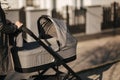 Back view of mother walking with her baby in stroller. Grey stroller outside, sunset Royalty Free Stock Photo