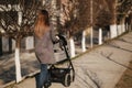 Back view of mother walking with her baby in stroller. Grey stroller outside, sunset Royalty Free Stock Photo