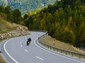 Back view of motorcyclist in black jacket and helmet riding sportbike along twisty road between tall green trees and beautiful