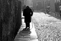 Back view of old man with hat and stick walking alone in city street during cold winter day in italian town