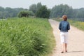 Back view of an old woman walking on the road near with grasses on the side Royalty Free Stock Photo