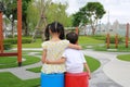 Back view of Older sister hugs little brother by the neck, shoulders sitting in playground in the garden with looking outdoor at