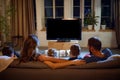 Back view of parents and children spending evening together, sitting on couch in living room and watching tv, eating Royalty Free Stock Photo