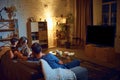 Back view of parents and children spending evening together, sitting on couch in living room and watching tv, eating Royalty Free Stock Photo