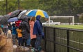 Back view of people with umbrellas standing under rain at a stadium waching football. Heavy rain, people under umbrellas