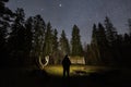 Back view of a person with flashlight standing in a forest clearing under a bright starry sky at night time Royalty Free Stock Photo