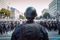 Back view of police officer with helmet and blurry crowd of protesting people in background