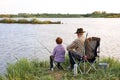Back view portrait of adult man and teenage boy sitting together on lake fishing with rods Royalty Free Stock Photo