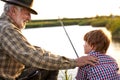 Back view portrait of adult man and teenage boy sitting together on lake fishing with rods Royalty Free Stock Photo