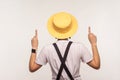 Back view portrait of female in hat and earrings, wearing white T-shirt and overalls, pointing up copy space. studio shot Royalty Free Stock Photo