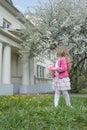 Back view portrait of little girl at classic portico and fruit tree garden in full bloom background