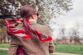 Back view of stylish woman wearing red hair scarf in spring park. Retro female fashion. Headscarf for bun hairstyle Royalty Free Stock Photo