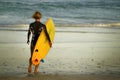 Back view portrait of young happy surfer girl walking towards the sea carrying yellow surf board and ready for surfing enjoying su Royalty Free Stock Photo