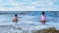 Back view of preteen boy brother, little girl sister siblings family sitting playing in water on beach near foamy waves. Royalty Free Stock Photo