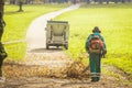 Back view of a public worker using leaf blower to clean path in a park from fallen leaves. Autumn scene in park Royalty Free Stock Photo