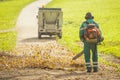 Back view of a public worker using leaf blower to clean path in a park from fallen leaves. Autumn scene in park Royalty Free Stock Photo