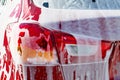 Back view of red compact SUV car with sport and modern design washing with soap. Car covered with white foam. Royalty Free Stock Photo