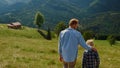 Back view father son walking on green hill. Parent with boy going down slope. Royalty Free Stock Photo