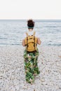 Back view of relaxed caucasian woman with yellow backpack and walking by the beach during sunset. summer time. daydreaming. Royalty Free Stock Photo