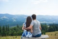 Back view of Romantic young couple enjoy the view of the mountains sitting on a bench on a sunny day in Carpatians. Royalty Free Stock Photo