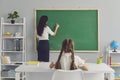 Schoolgirl sitting at desk and looking at teacher writing elementary sum on board Royalty Free Stock Photo