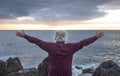 Back view of a senior man enjoying freedom standing in front to the sea at sunset with open arms, cloudy sky - horizon over water Royalty Free Stock Photo