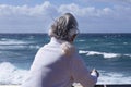 Back view of a senior woman with wind in the hair looking at the horizon over water. Active elderly retiree in winter holiday Royalty Free Stock Photo