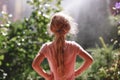 Back view of seven years old blonde girl wearing pyjamas standing outdoor in home garden in the early morning