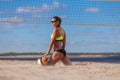 Back view of sexy athletic girl in a swimsuit and sunglasses touches a ball while sitting on the sand next to a beach Royalty Free Stock Photo